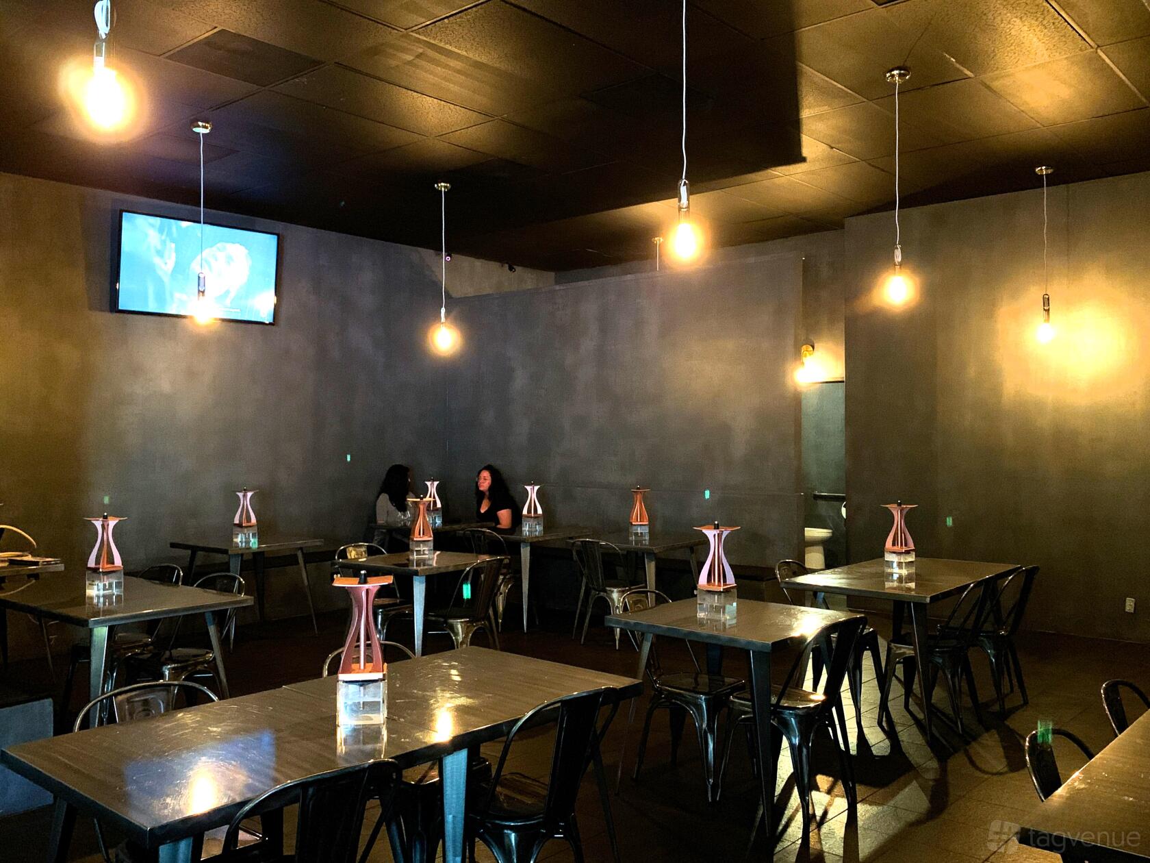 A lounge in a bar with exposed bulb lighting, gray walls, and square tables at Boba Bear Rowland Heights.