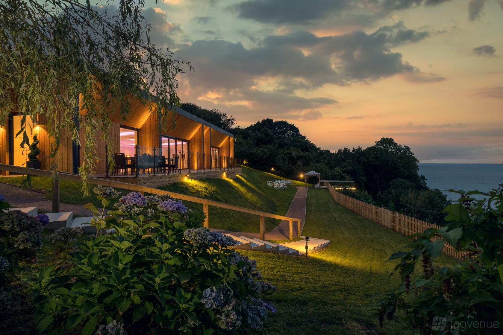A hotel with a modern wood exterior, large glass windows, and landscaped gardens overlooking the sea at The Venue At Sandy Cove.