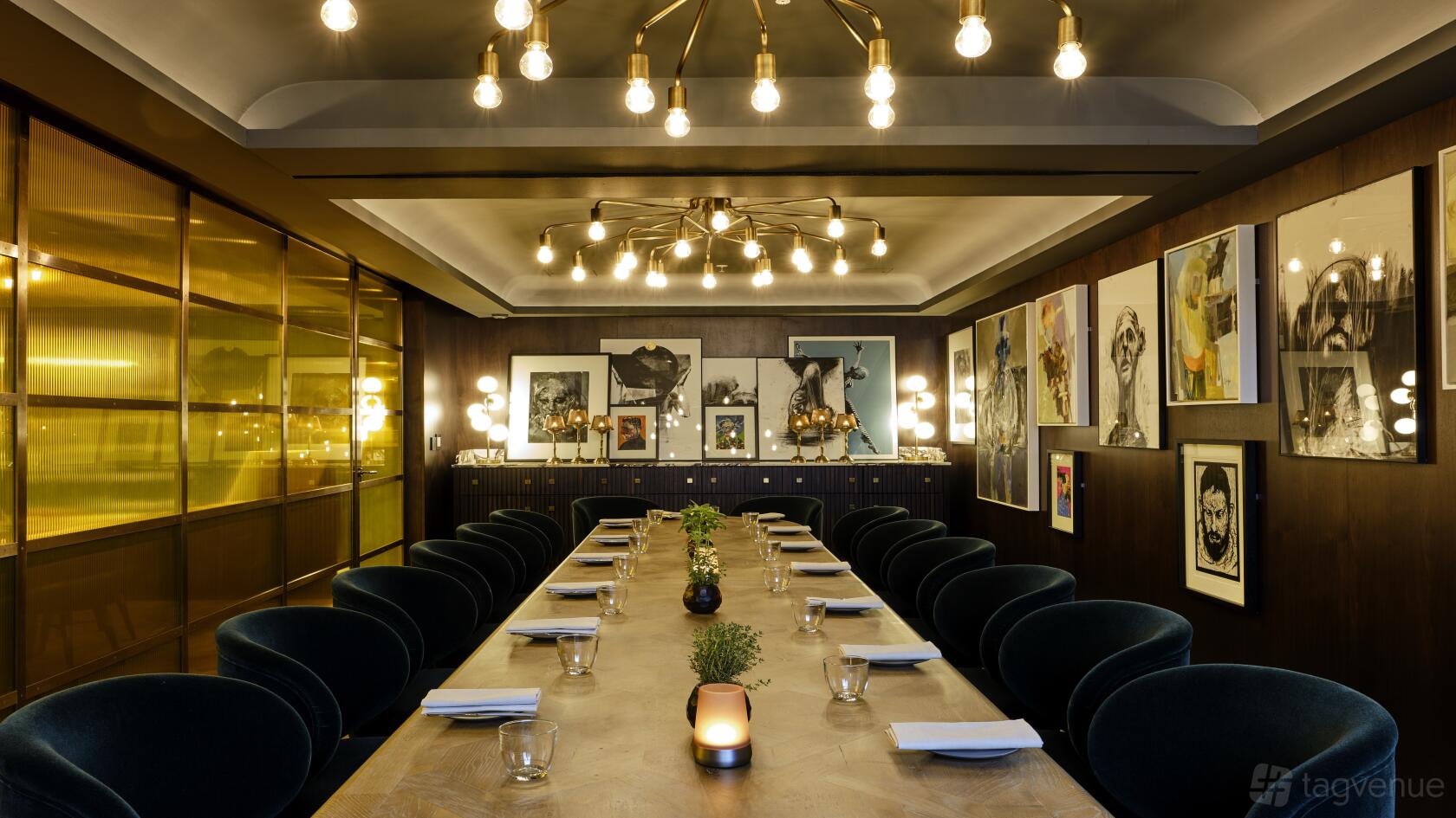 A dining room with velvet chairs, a long wooden table, gallery wall of framed art, and pendant lighting at Wild Honey St James.