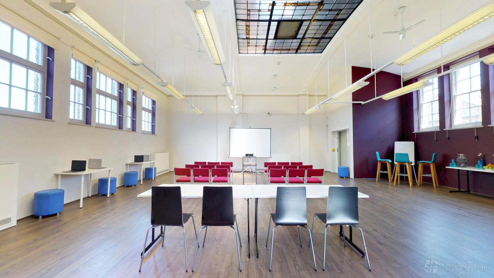 A function room with rows of red chairs, high windows, and a ceiling skylight at The Upper Norwood Library Hub.