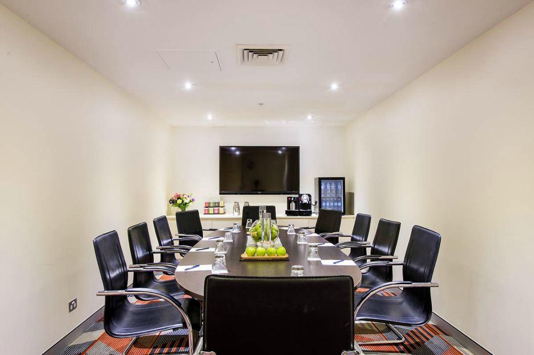 A hotel boardroom with a long conference table, black leather chairs, and a wall-mounted TV at Sydney Central Hotel.
