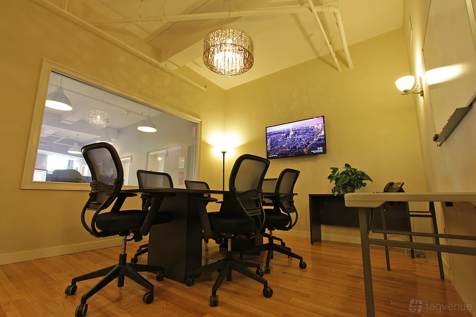 A meeting centre with a rectangular conference table, ergonomic chairs, wall-mounted TV, and hardwood floors at Select Office Suites Flatiron.