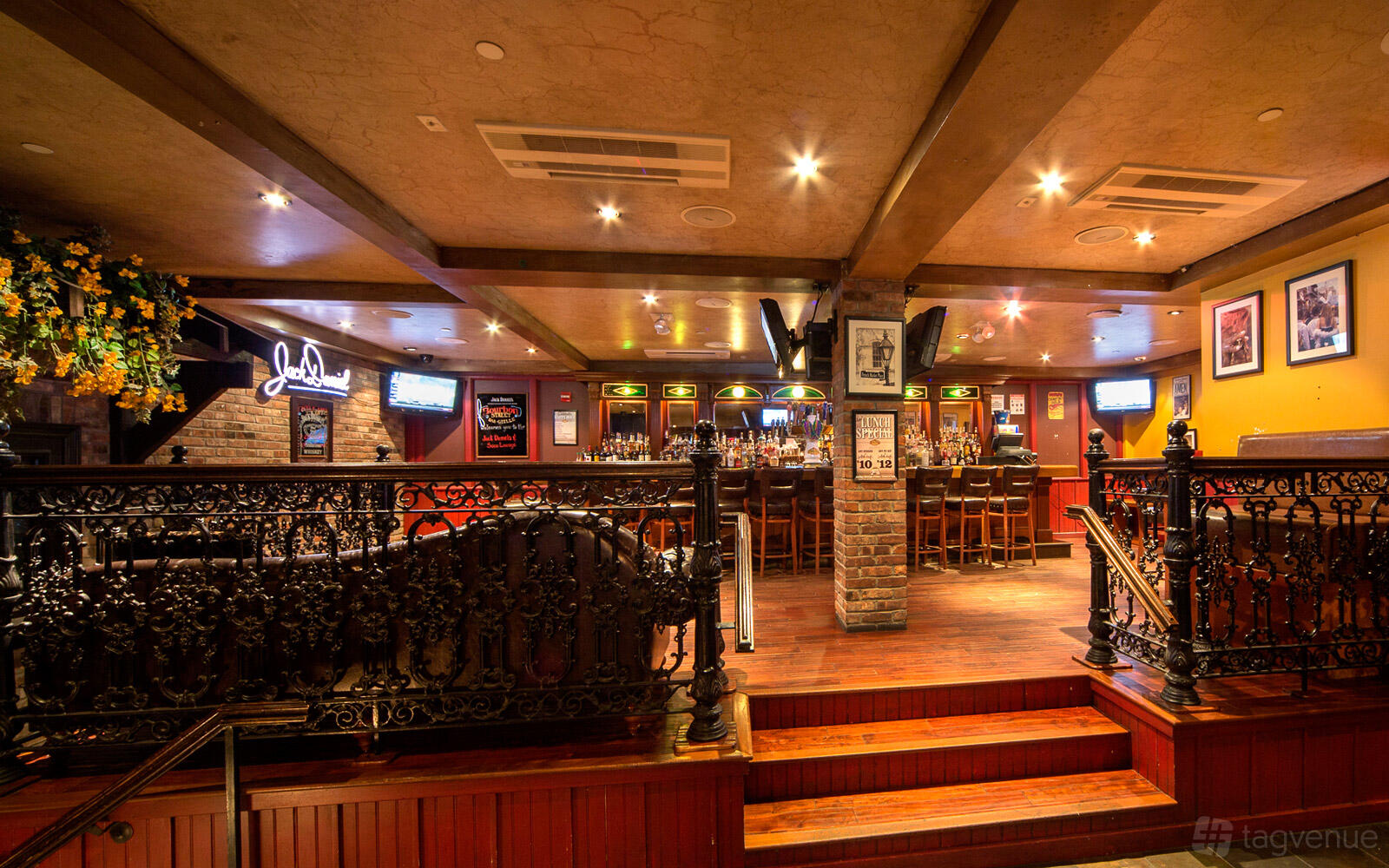 An event space in a restaurant with dark wood floors, ornate iron railings, and a central bar at Backstage Tavern.