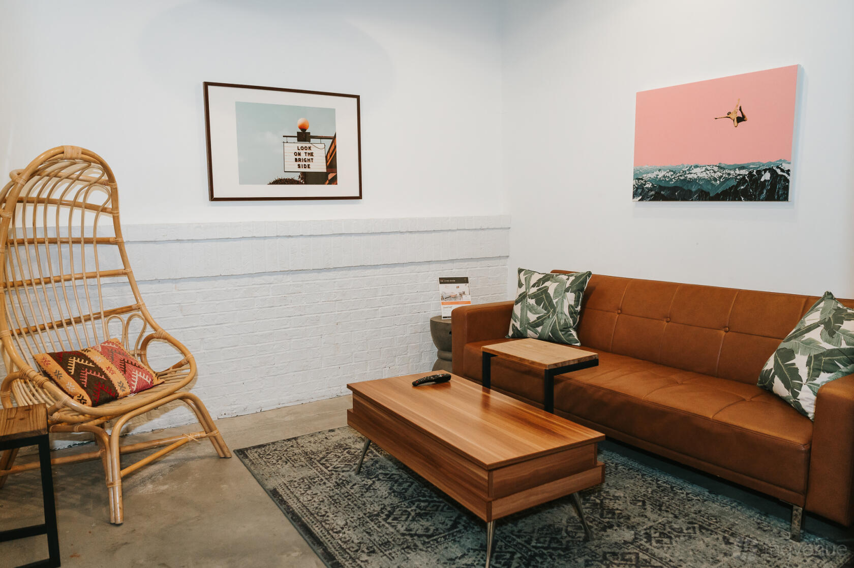 An event space with a brown sofa, rattan chair, patterned rug, and wall art at THRIVE - Alpharetta.