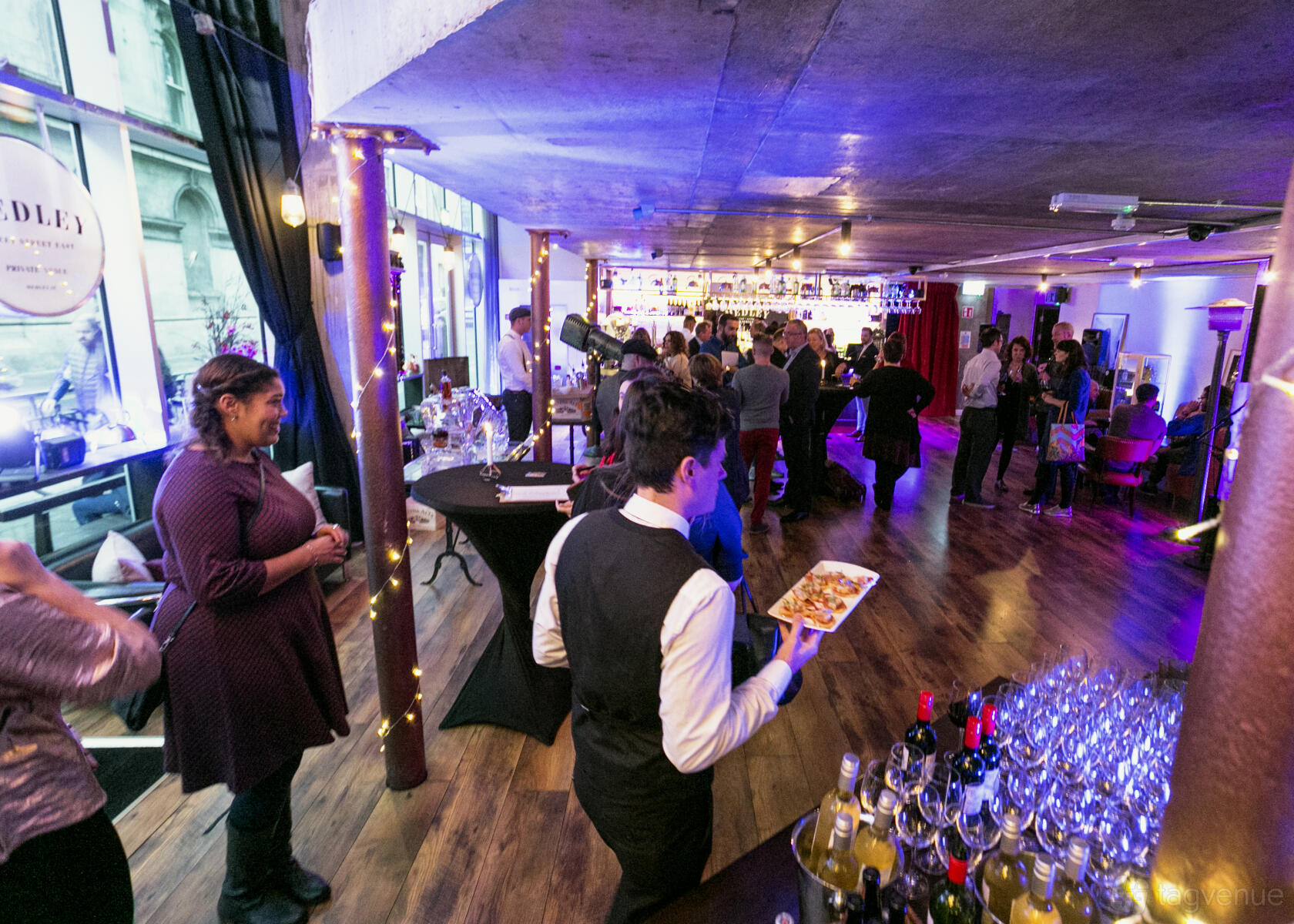 An event space in a restaurant with wood floors, round cocktail tables, and festive string lights at Medley.