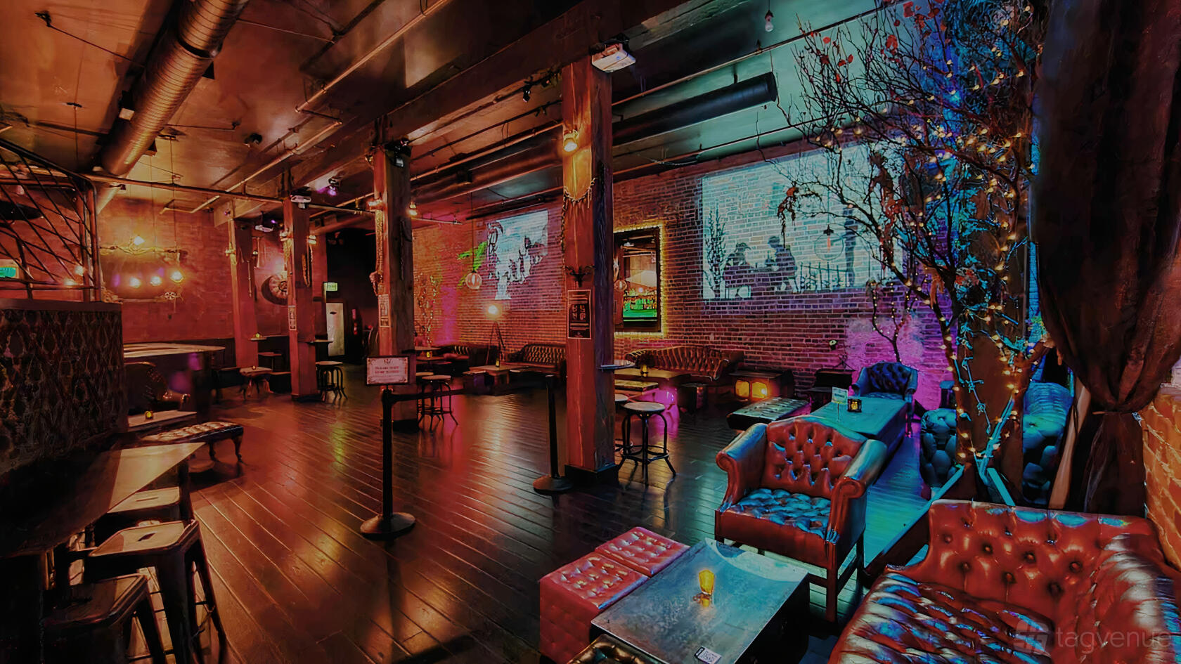 A cocktail bar with exposed brick walls, leather sofas, dark wood floors, and colorful accent lighting at Alchemist Bar & Lounge.