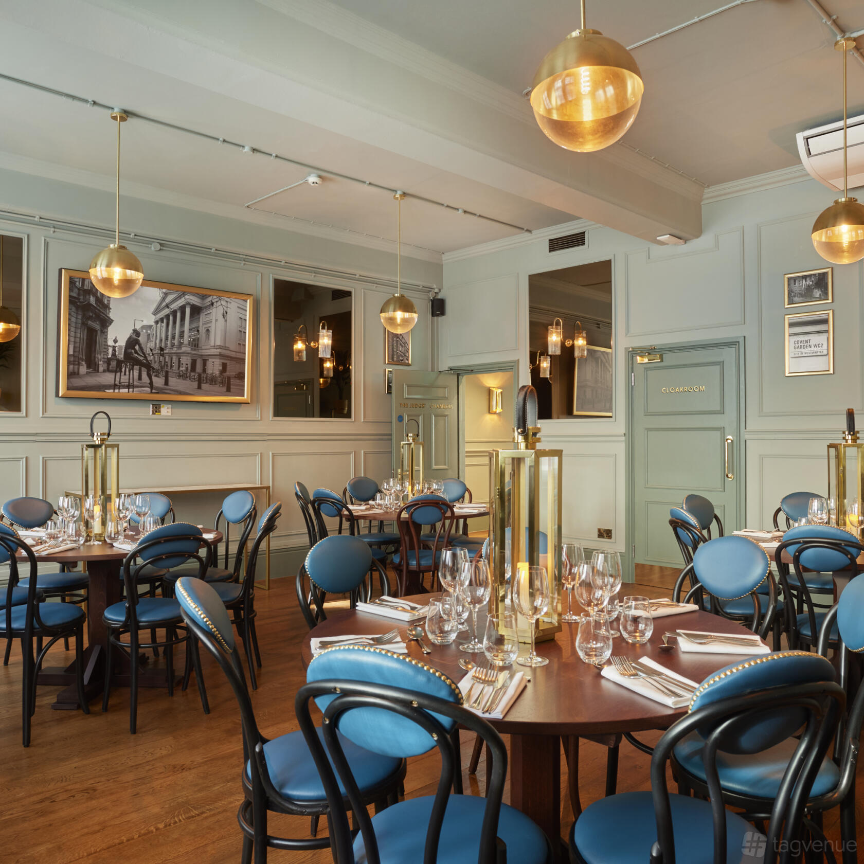 A function room in a restaurant with elegant blue chairs, round tables set with glassware, and pendant lighting at Browns Covent Garden.