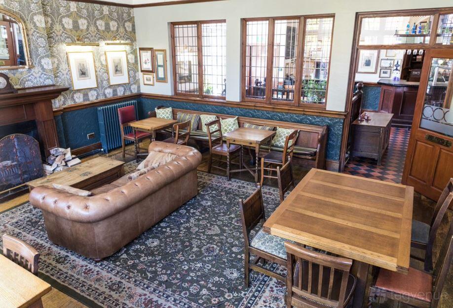 A function room in a pub with patterned wallpaper, a leather sofa, wooden tables, and a fireplace at The Metropolitan, West Didsbury.