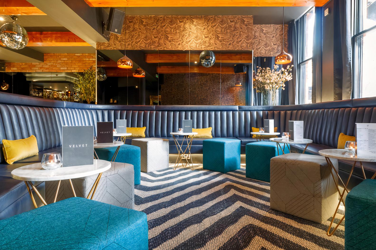 An event space in a hotel with velvet banquette seating, geometric ottomans, and marble tables at Velvet Hotel, Bar & Brasserie.