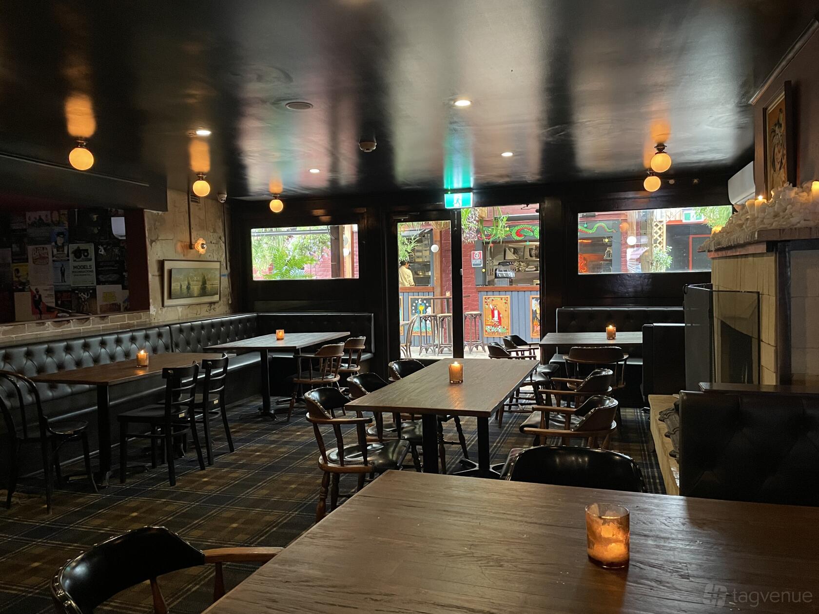 An event space in a bar with dark wood tables, plaid carpet, leather banquette seating, and a fireplace at The Duke of Enmore.