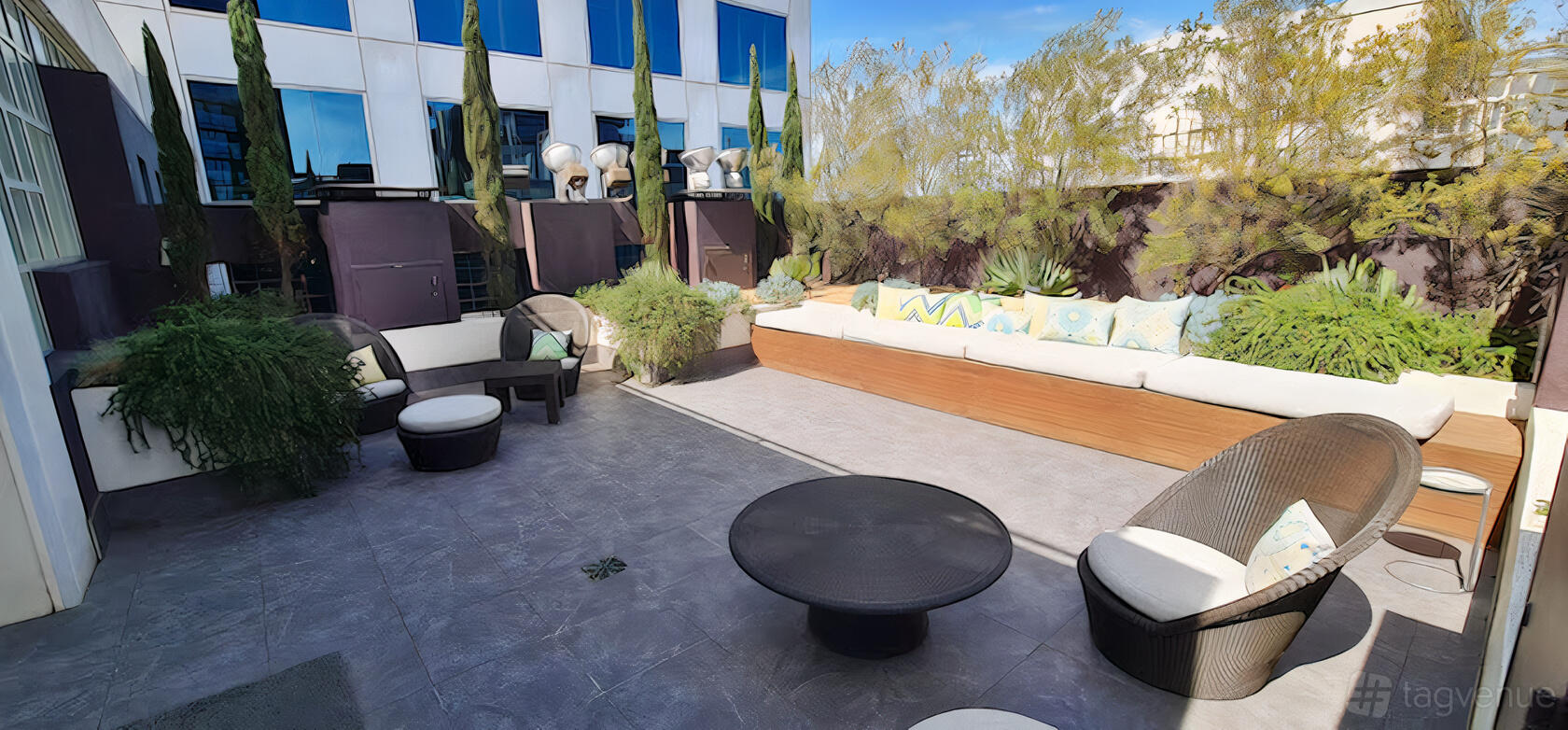 An outdoor hotel sun deck with cushioned bench seating, round wicker chairs, and potted greenery at The Como Melbourne.