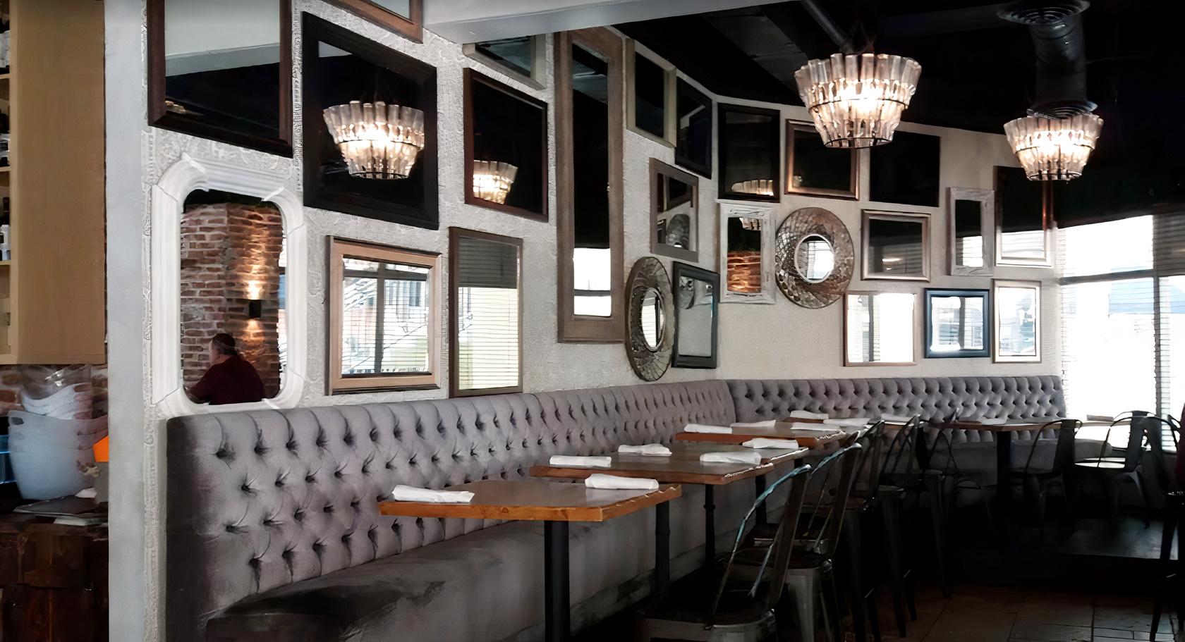 A bar with tufted banquette seating, wood tables, and a wall covered in assorted mirrors at Candela Bar Brickell.