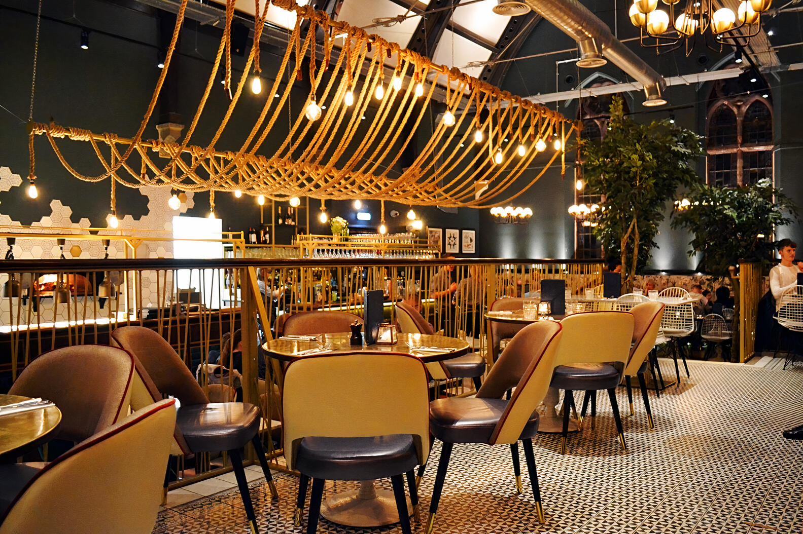 An event space in a restaurant with hanging rope lights, patterned tile flooring, and gold-accented chairs at The Lost and Found Knutsford.