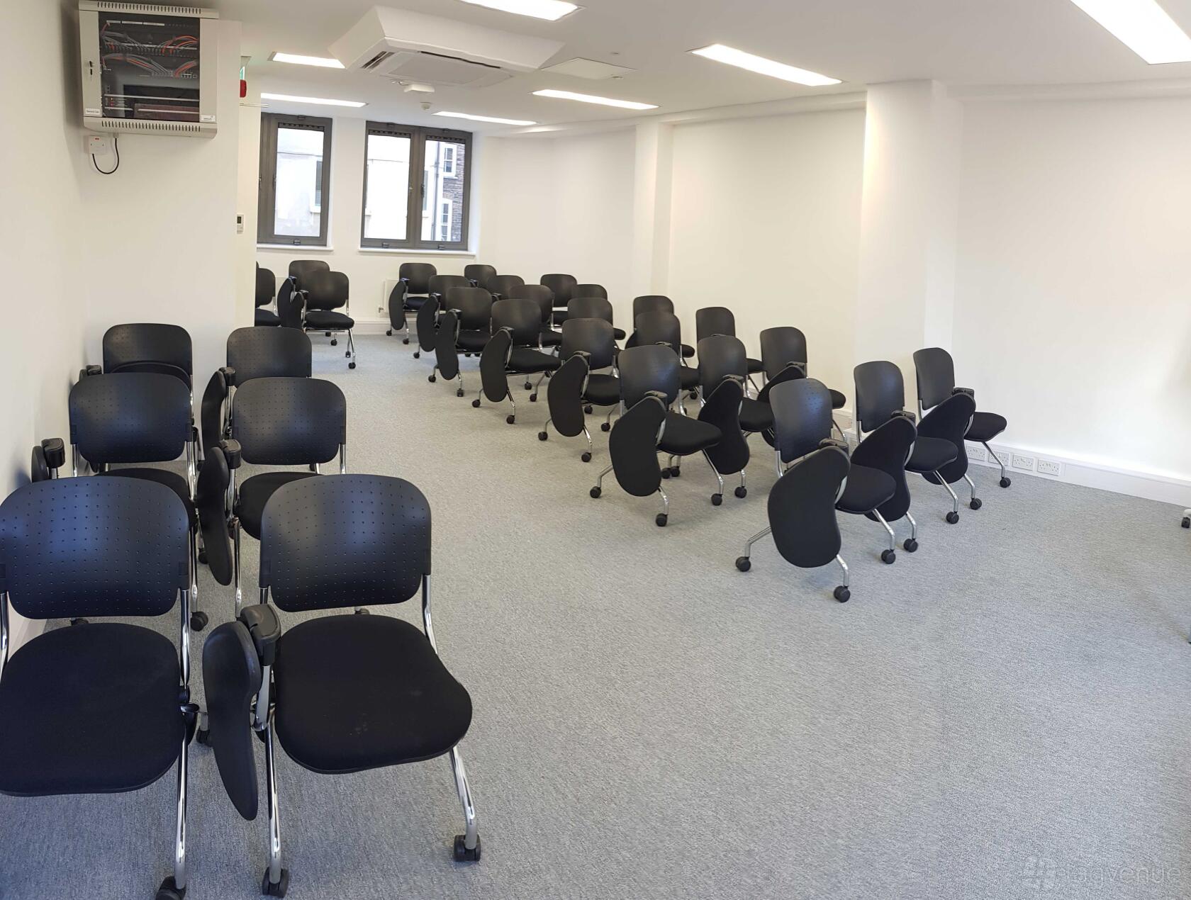 A classroom with black chairs on casters arranged in rows and large windows at Richbell House.