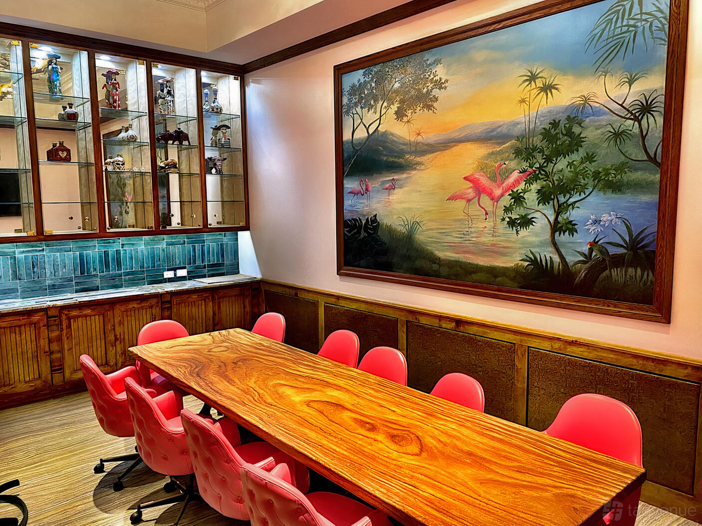 A restaurant with a long wooden dining table, pink chairs, and a tropical mural at La Viva.