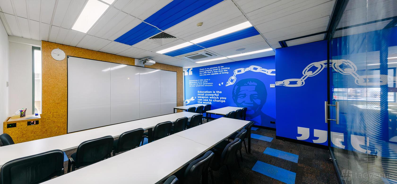 A classroom with long white tables, black chairs, wall art, and a large whiteboard at Hurstville Learning Centre.
