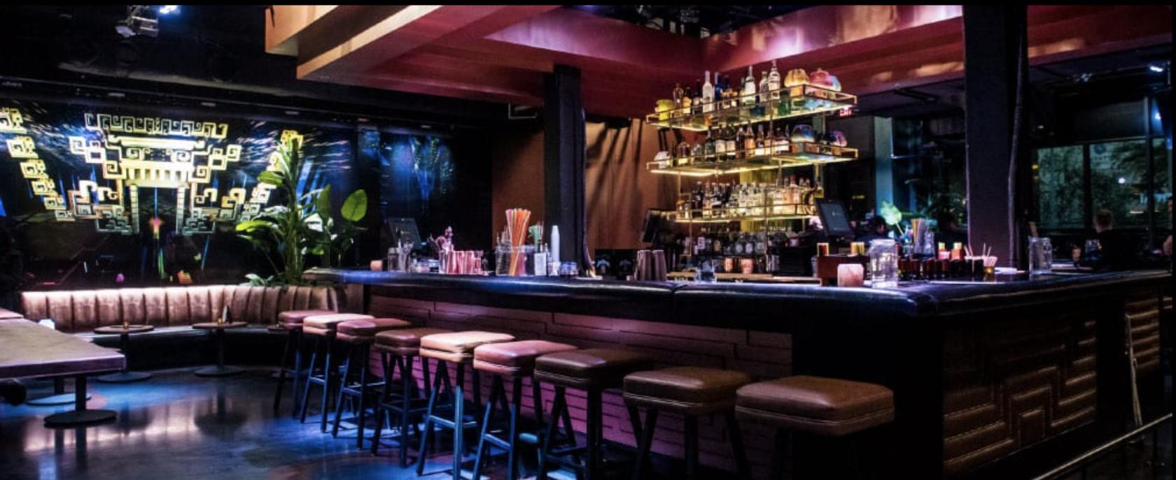 A bar event space with backlit shelving, high-top stools, and leather seating at Merkaba.