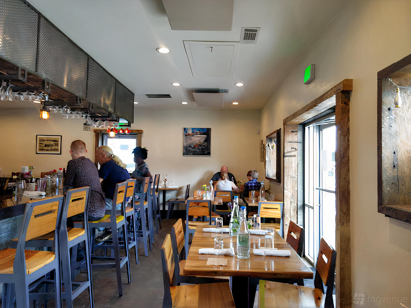 A restaurant dining room with wooden tables, high-backed chairs, and a bar area at Petit Chou.