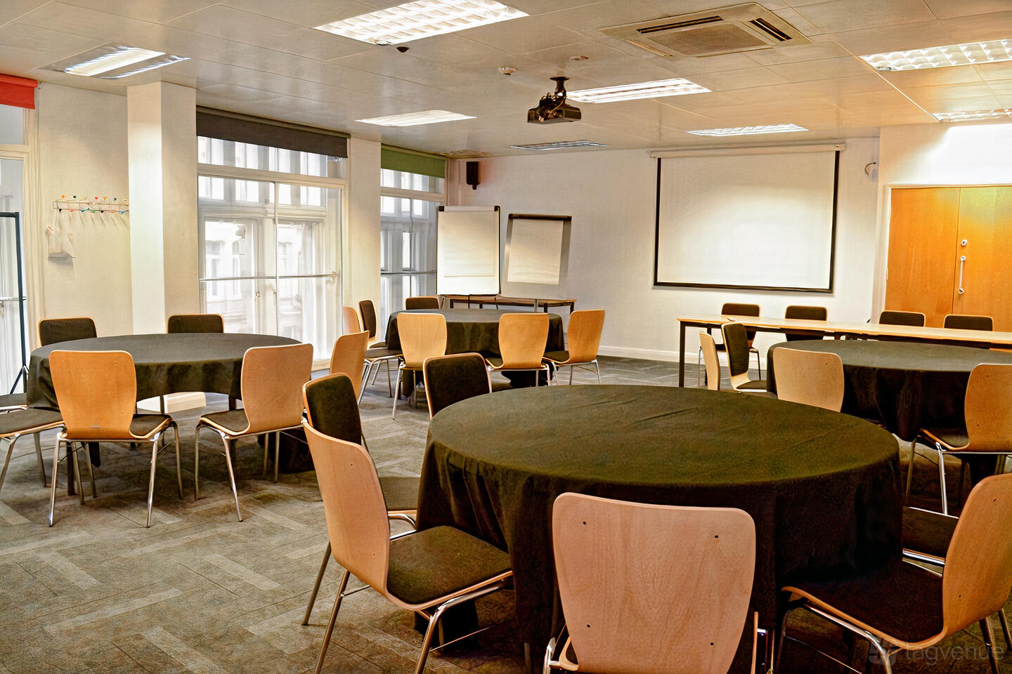A meeting centre with round tables covered in black cloths, flipcharts, and a projector at The Studio Birmingham.