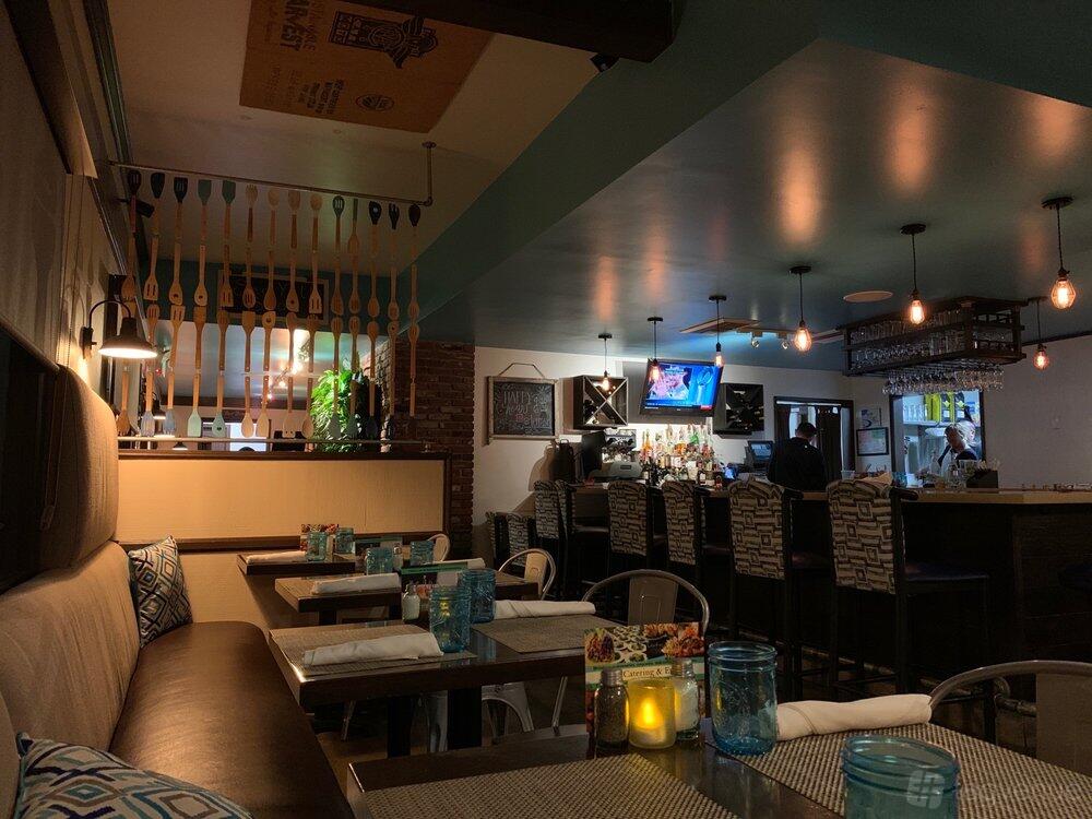 A restaurant with cushioned bench seating, patterned chairs, and a bar with hanging glasses at Terra American Bistro.