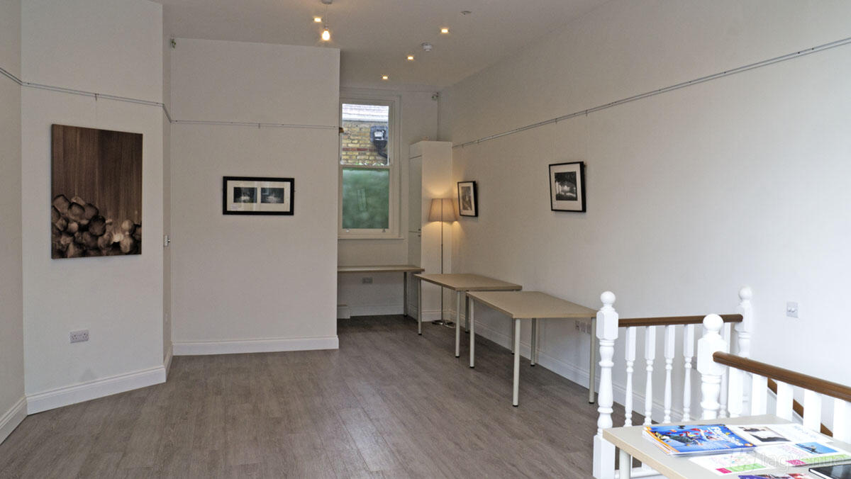 An event venue with light wood floors, white walls, framed art, and a window at The Living Room Place Furzedown Venue.