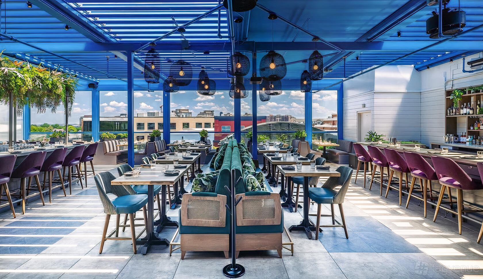 A rooftop restaurant with a blue pergola, hanging pendant lights, greenery accents, and city views at Buena Vida Gastrolounge.