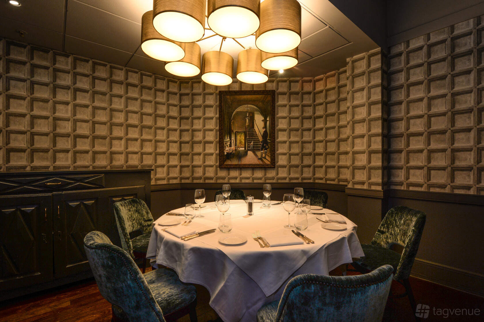 A dining room with a round table set for six, velvet chairs, and textured paneled walls at Balls Brothers Minster Court.