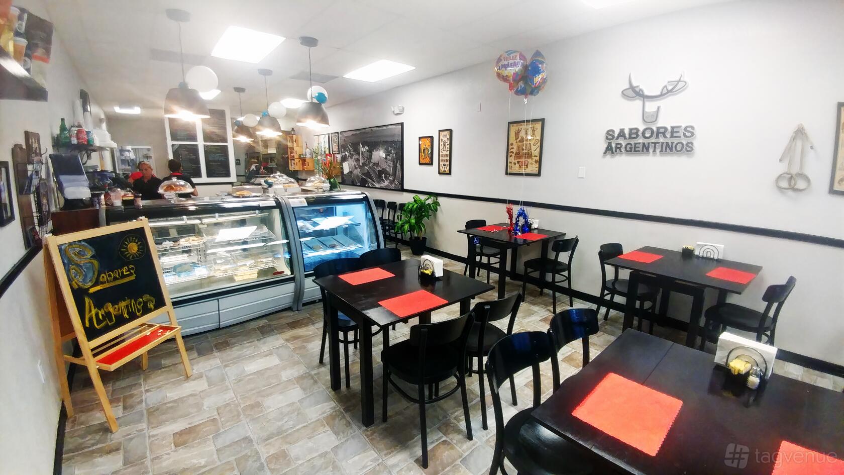 A restaurant with black tables, red placemats, wall art, and a display counter at Sabores Argentinos.