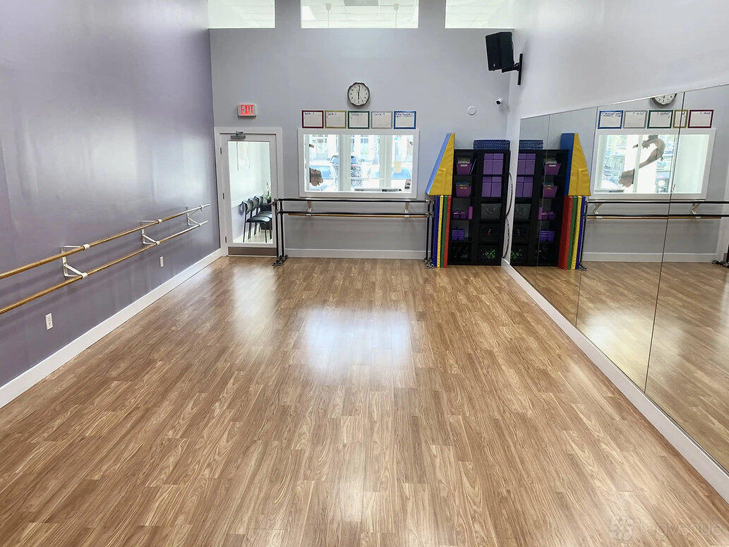 A dance studio with wooden floors, mirrored wall, ballet barres, and storage cubbies at Creativo Dance Studio - 82nd Ave.