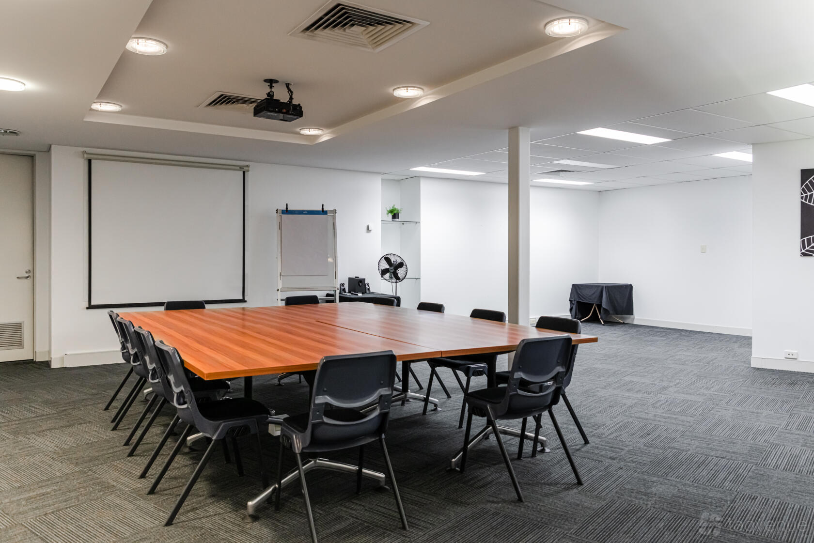 A boardroom with a large wooden meeting table, black chairs, projector, and screen at BTP Conference & Exhibition Centre.