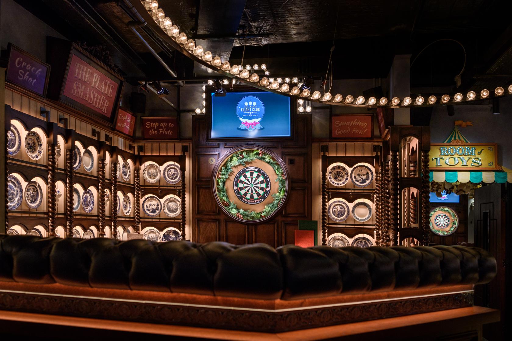 A pub with multiple dartboards, carnival-style lights, and tufted leather seating at Flight Club Victoria.