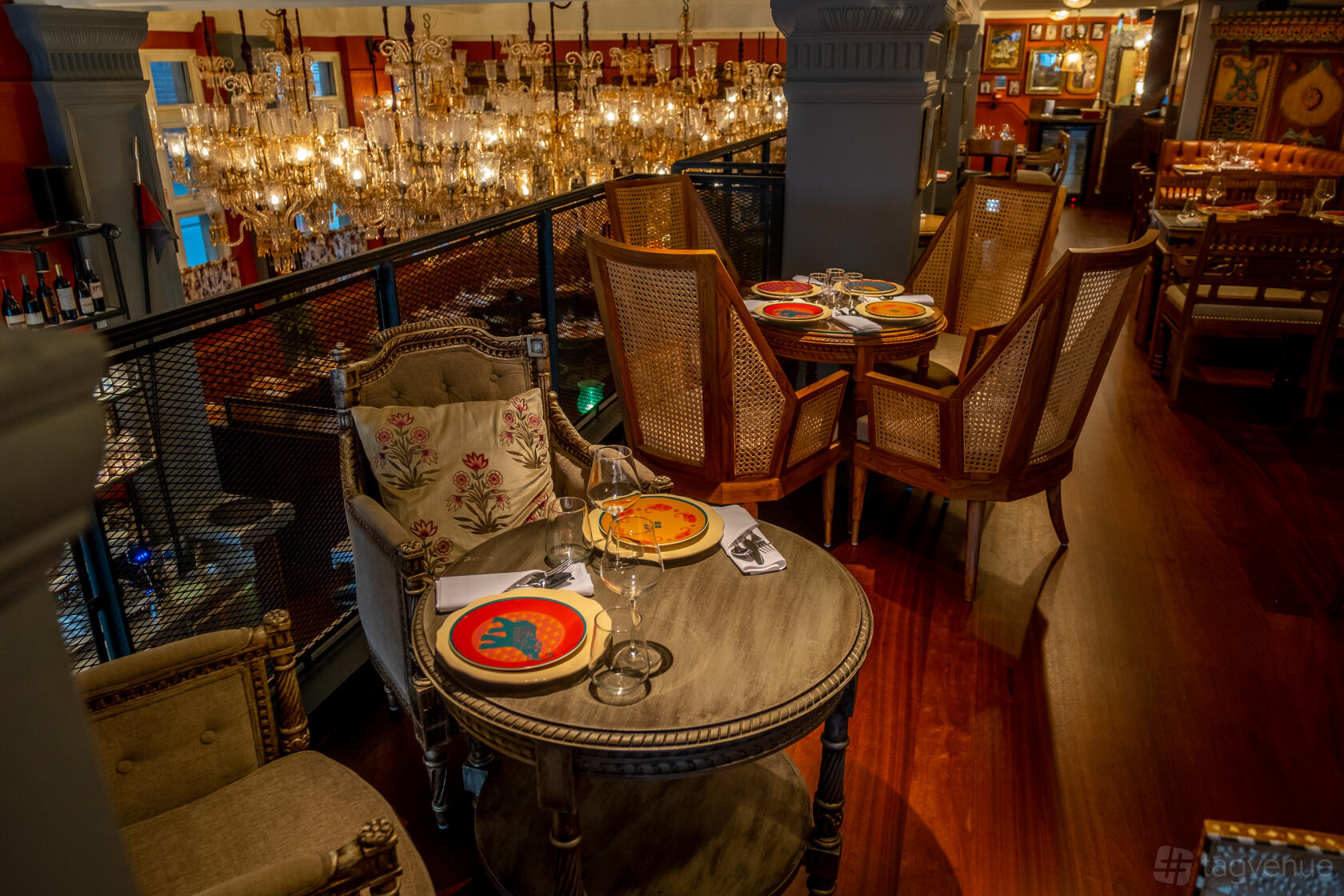 An event space in a restaurant with ornate chandeliers, wooden floors, and cane-back chairs at Colonel Saab Mezzanine.