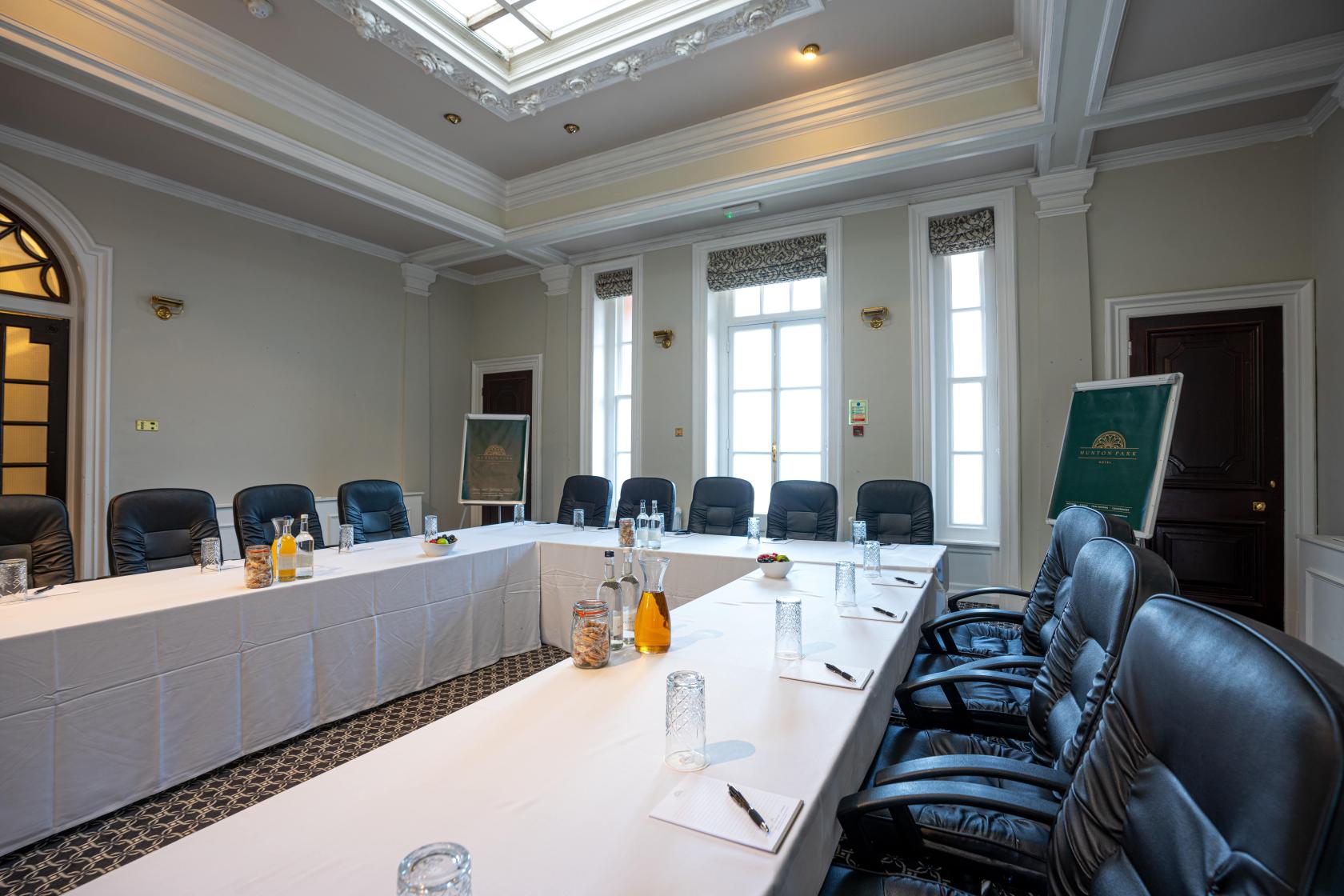 A meeting room with U-shaped white-clothed tables, black leather chairs, and natural light at Hunton Park Hotel.