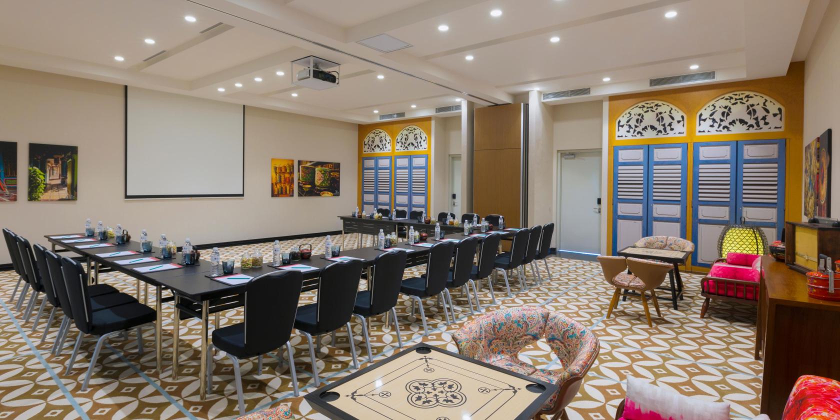 A meeting room with patterned tile flooring, long tables arranged in a U-shape, and decorative shutter panels at Hotel Indigo Singapore Katong.