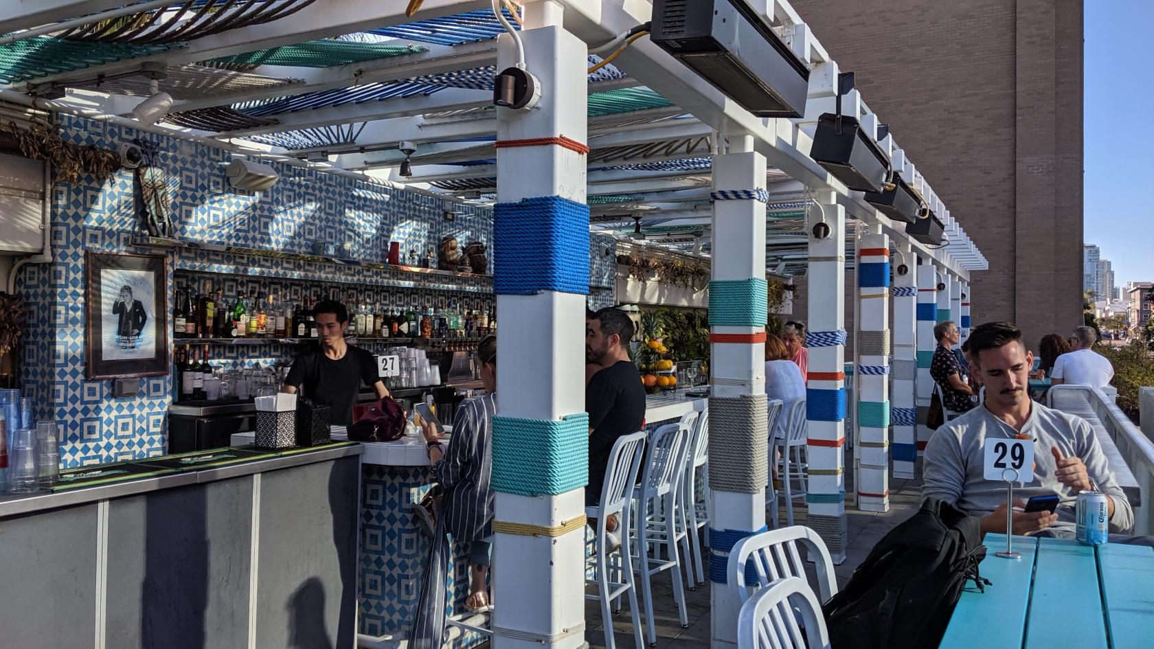 An outdoor event space in a bar with a tiled bar counter, high stools, and striped pillars at Fairweather Rooftop Bar.