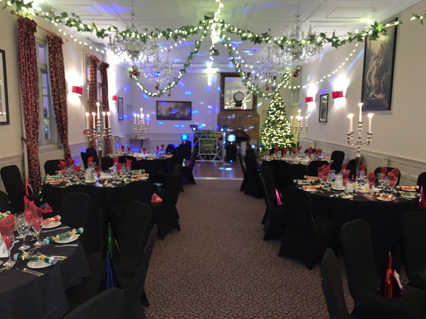 A function room with round tables dressed in black linens, candelabras, and festive string lights at The Talbot, Ripley