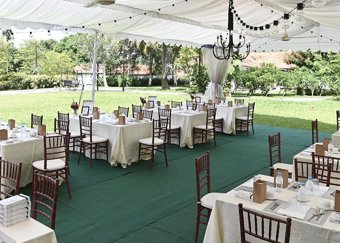 An outdoor event space with a white canopy, chandeliers, and round tables with wooden chairs at Bay Laurel.