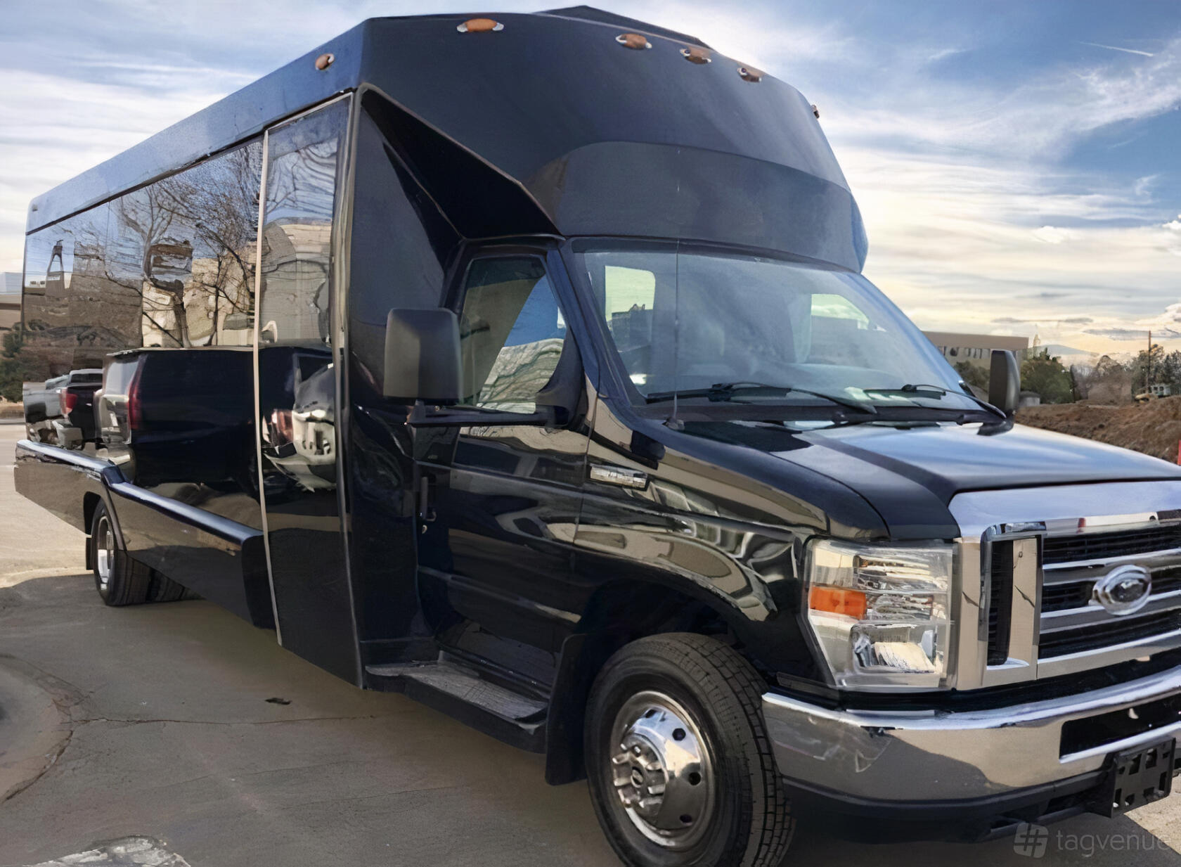 A black party bus with tinted windows and chrome accents parked outside at DFW Black Car Service LLC.