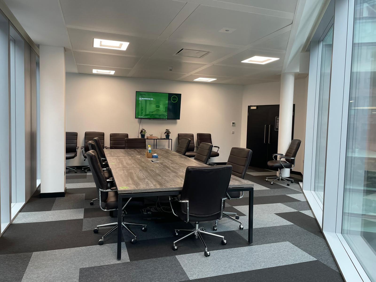 A boardroom with a long wood table, leather chairs, large windows, and a wall-mounted screen at Avenue HQ St Paul's Square.