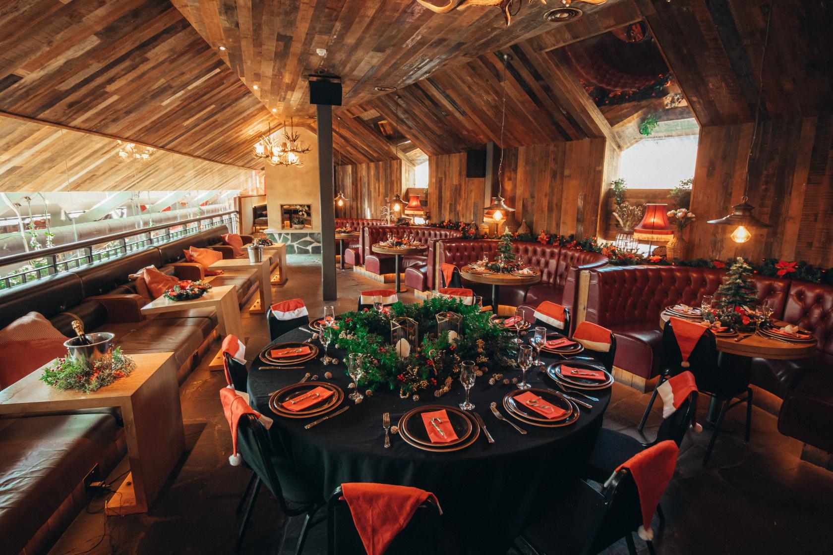 An event space in a bar with wood-paneled ceilings, round tables set with black linens, and red upholstered booths at Impossible Bar and Theatre.