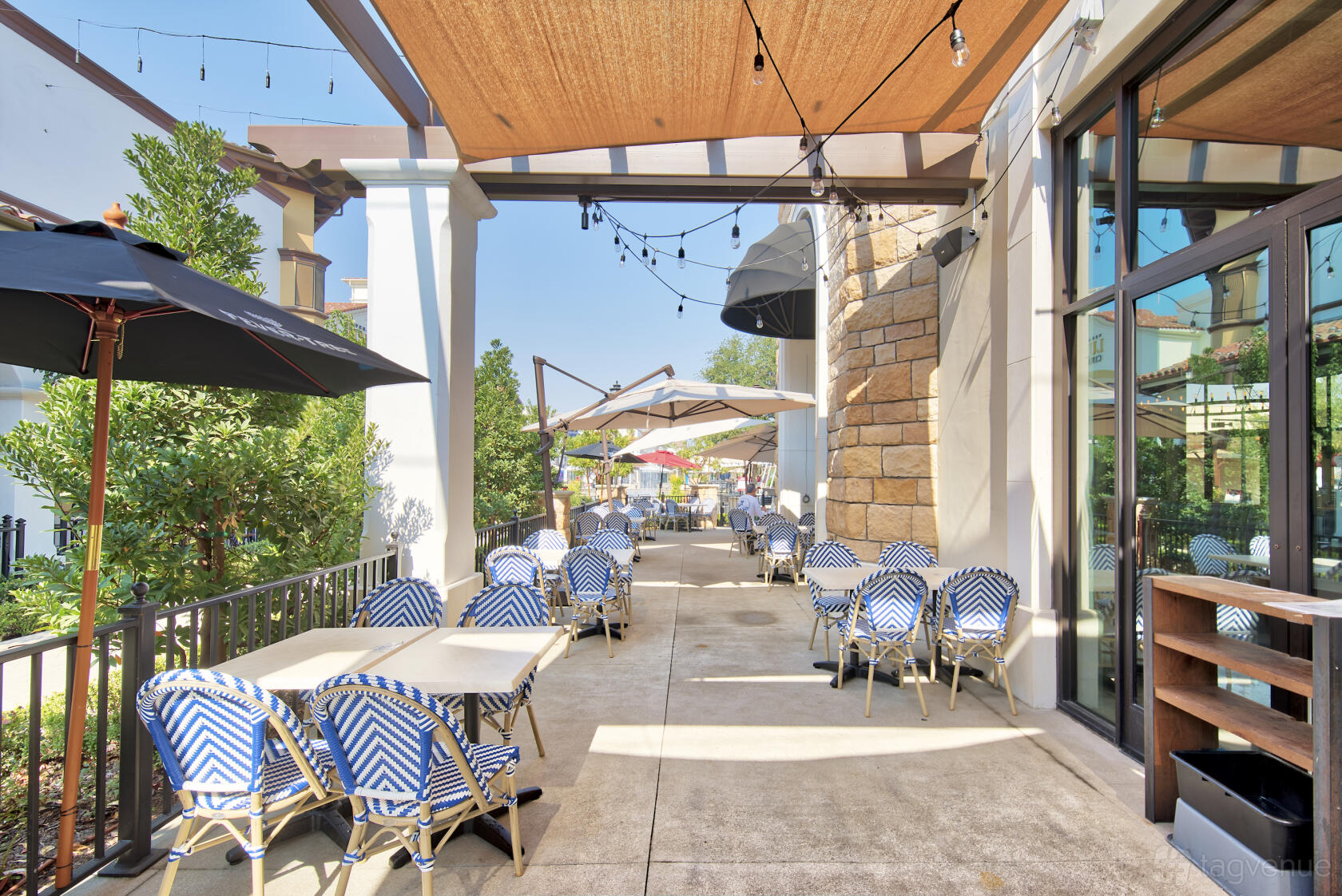 An outdoor dining area with blue and white chairs, string lights, and shade sails at Doppio Zero Concord.