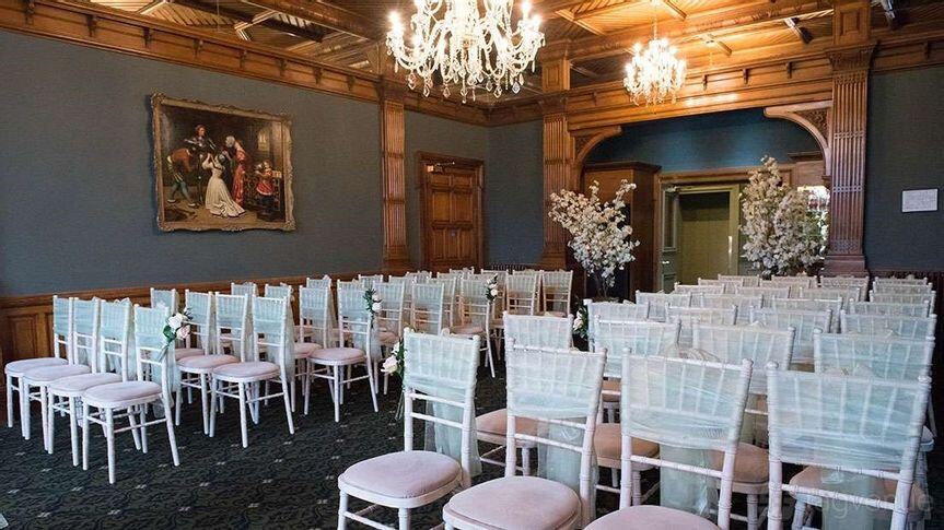 An event space with chandeliers, wooden paneling, and rows of white chairs with floral accents at Woodlands Park Hotel.