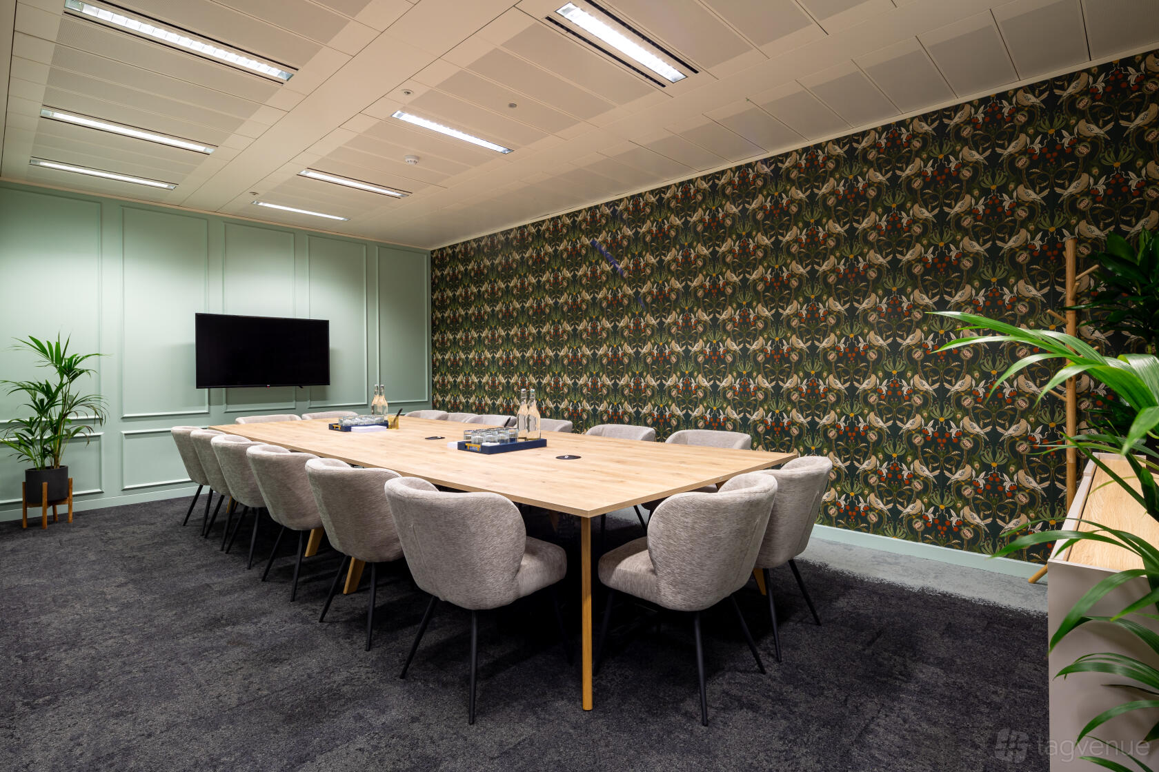 A meeting centre room with a long wooden table, upholstered chairs, patterned accent wall, and wall-mounted screen at Landmark: Cannon Street, London.