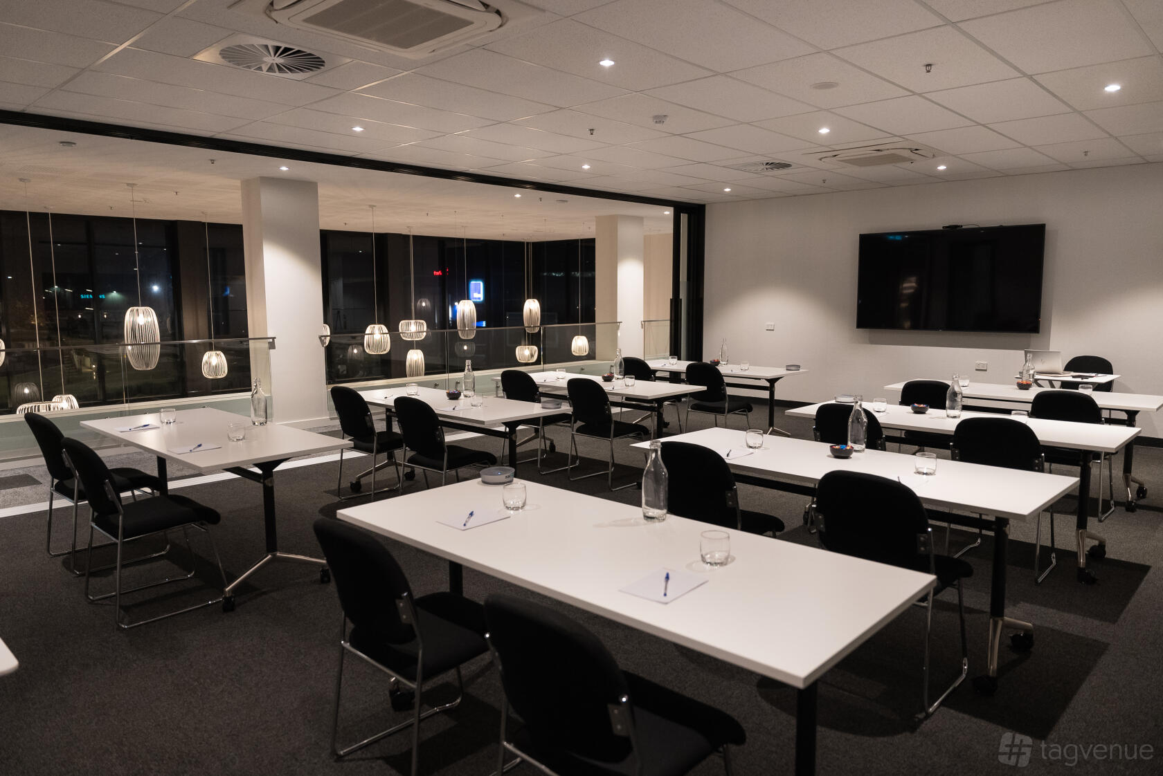 A hotel meeting room with rectangular tables, black chairs, glassware, notepads, and pendant lighting at Mantra Tonsley Adelaide.