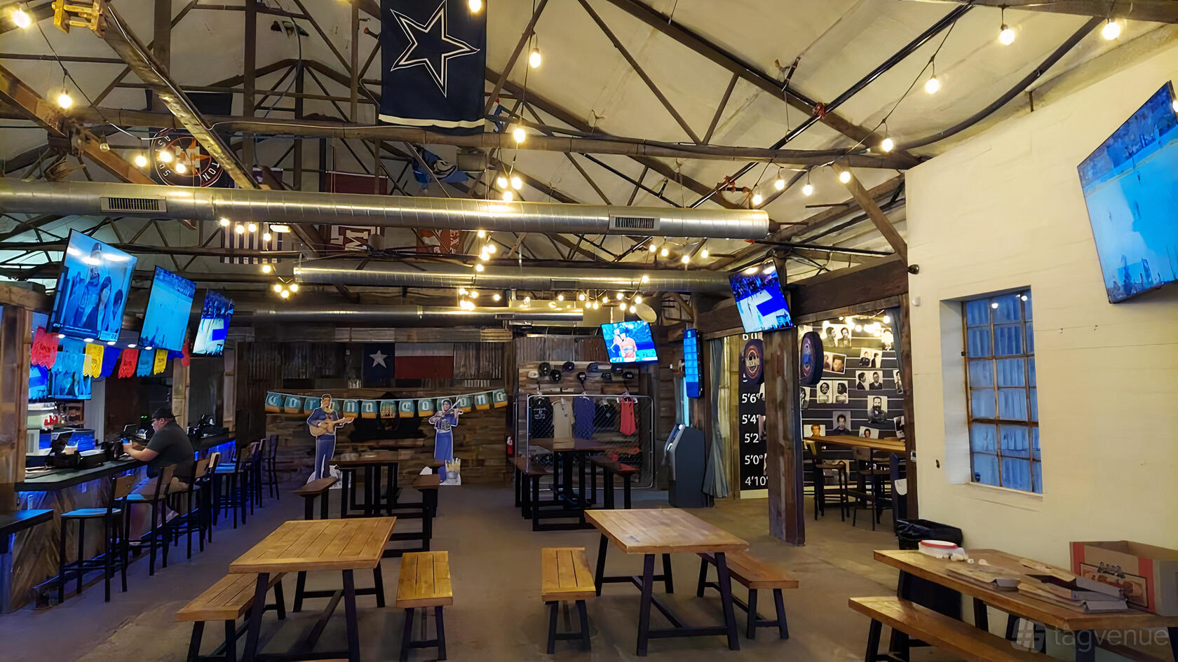 An event space in a bar with wooden tables, exposed beams, string lights, and sports décor at Side Door Cocktails & Coffee.