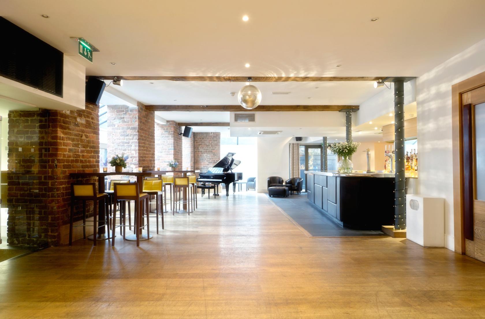 A hotel lounge with exposed brick walls, a grand piano, and tall wooden tables at Hope Street Hotel.