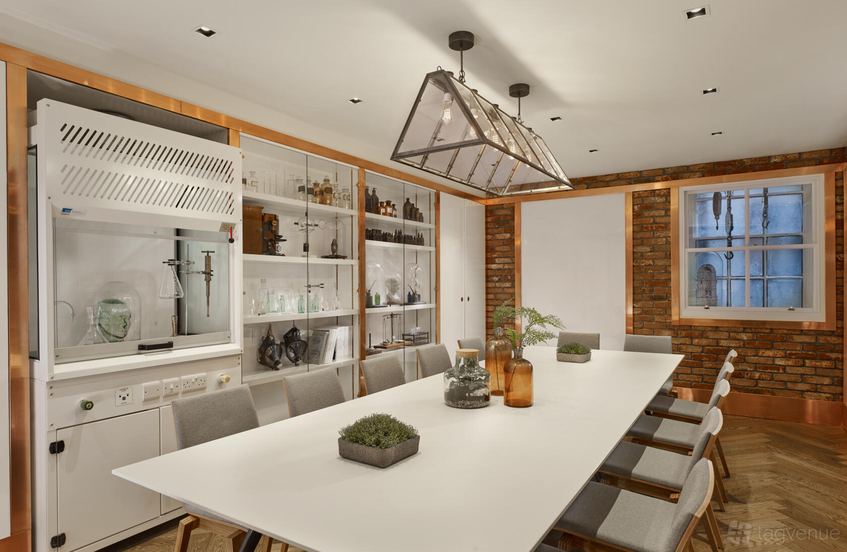 A dining room with a long white table, upholstered chairs, built-in glass cabinets, and exposed brick walls at The Residence at Holmes Hotel London.