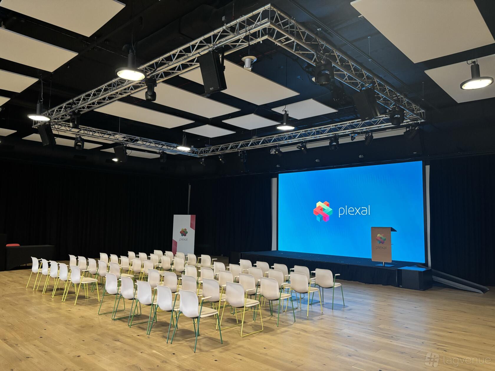 An event space with rows of white chairs, a wooden podium, and a large presentation screen at PLEXAL.
