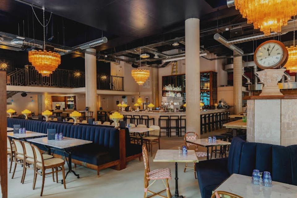 A bar in a restaurant with marble tables, velvet banquette seating, and amber chandeliers at Teatro Hall.