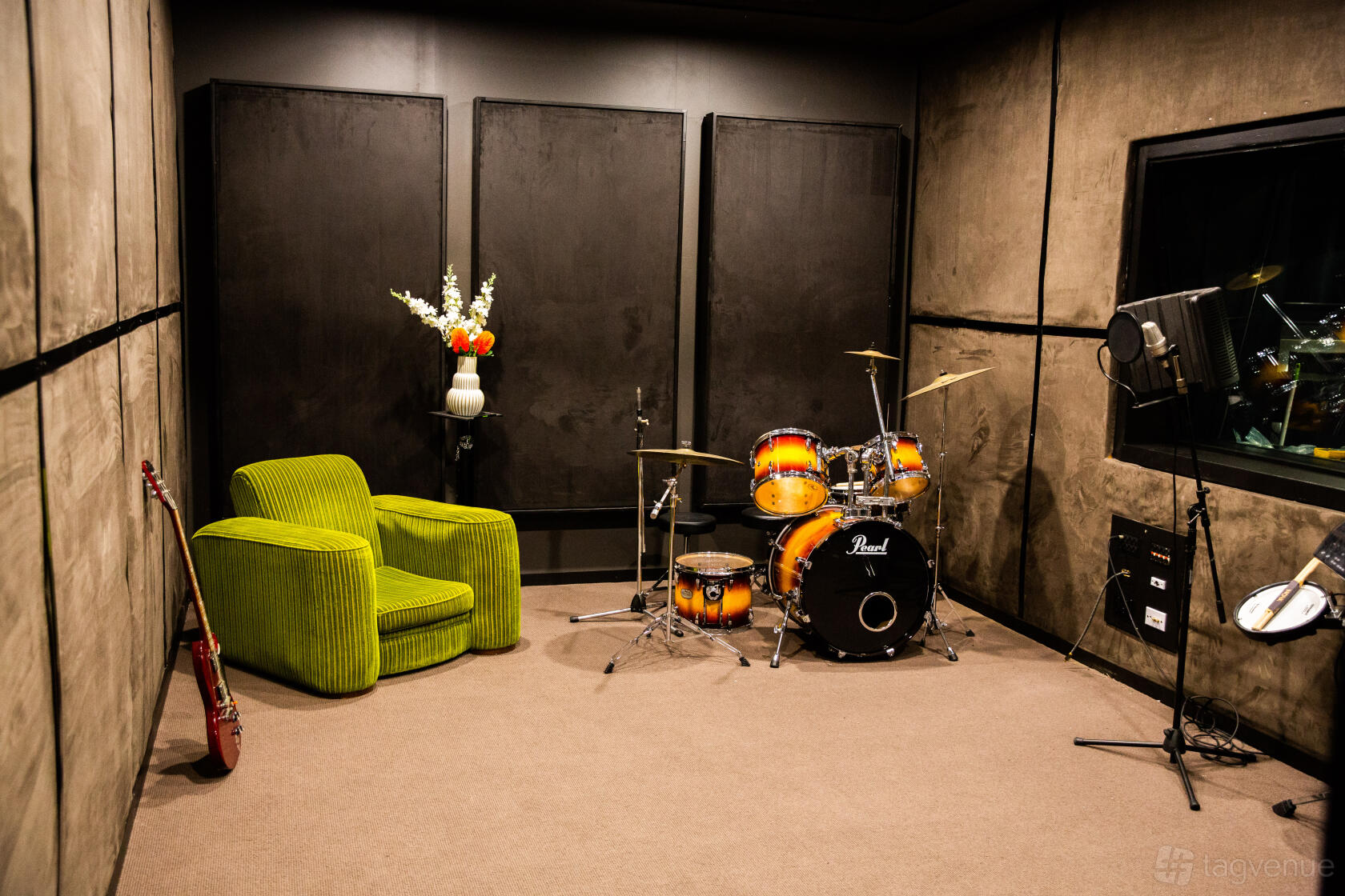 A music studio with a drum set, electric guitar, green armchair, studio lighting, and soundproofed walls at Focal House.